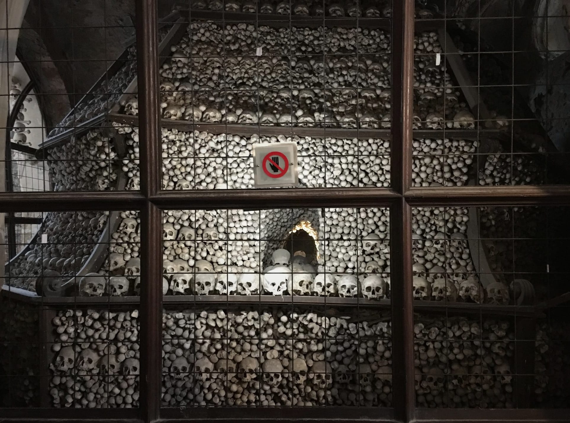 A decorative pile of human bones behind a fence with a sign that shows a hand with a line through it